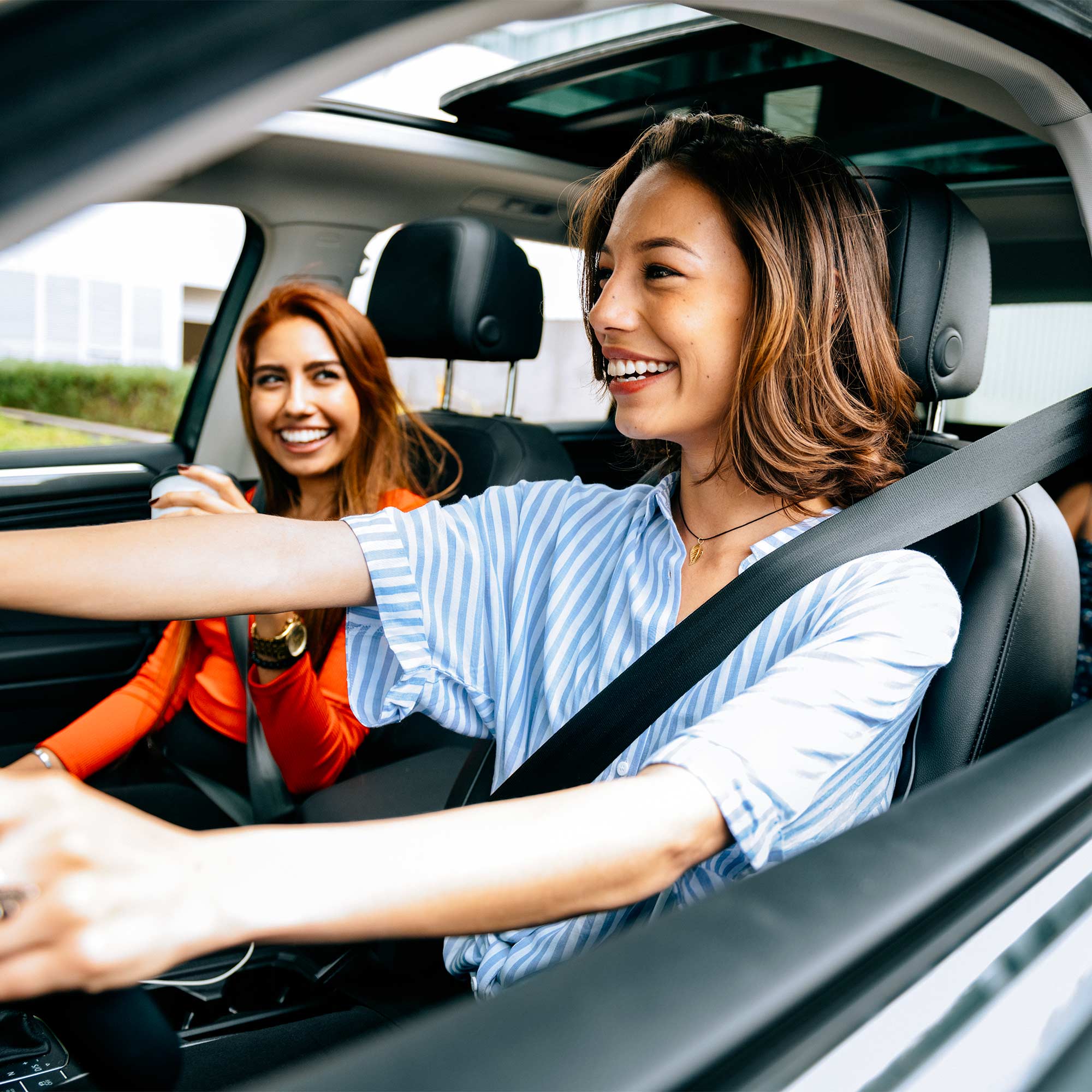 Two women smiling as they drive with the windows down.